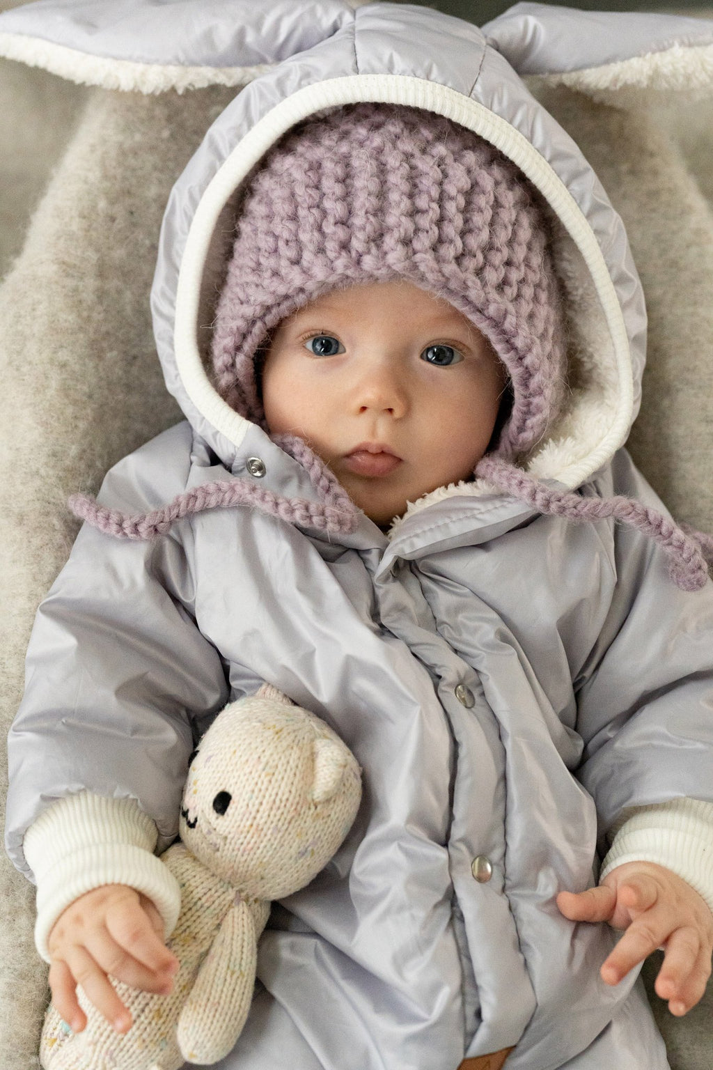 3. Close-up of baby in Zezuzulla winter jumpsuit with rabbit ears, wearing a knitted hat, emphasizing warm teddy lining and button details
