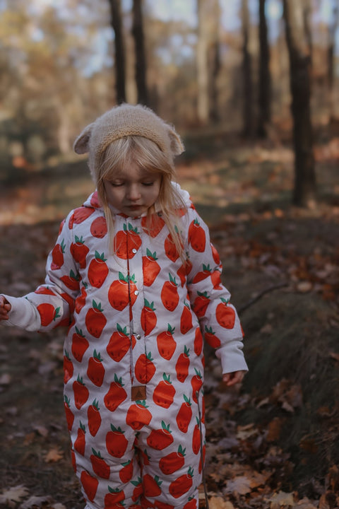 1. Child wearing Zezuzulla winter jumpsuit with strawberry print and teddy bear ears in a forest setting
