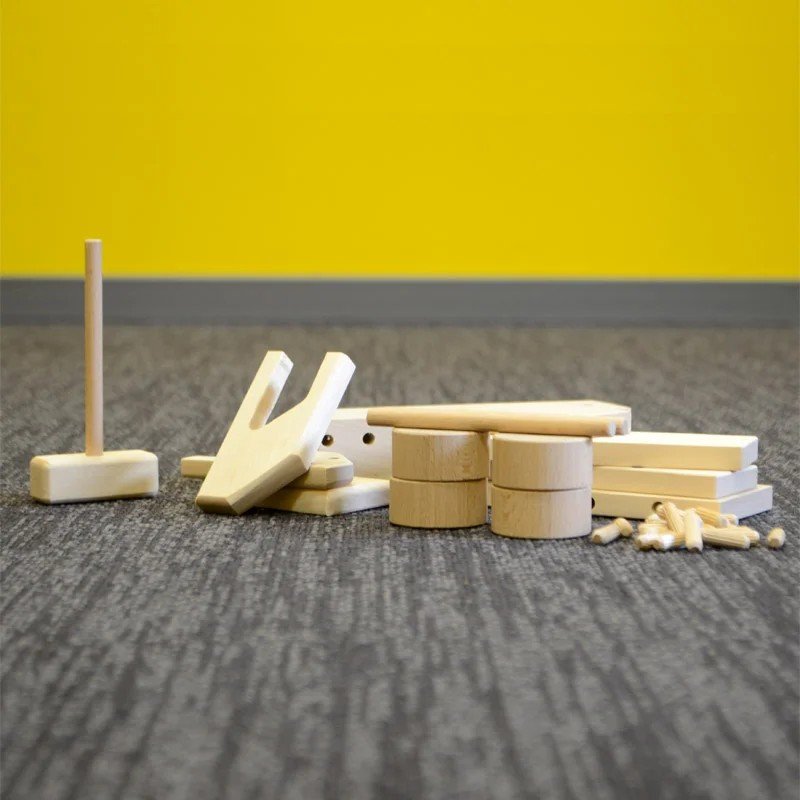 4. Flat lay of unassembled Adensen Villi wooden truck parts on a carpet with a yellow wall background