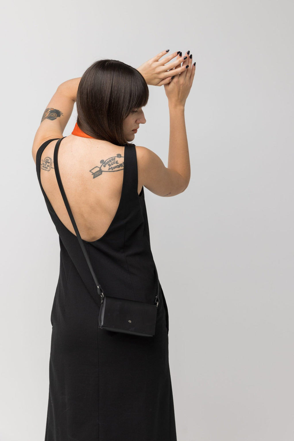 2. Back view of woman wearing PYKOK KORA minibag in black leather, paired with black dress in studio
