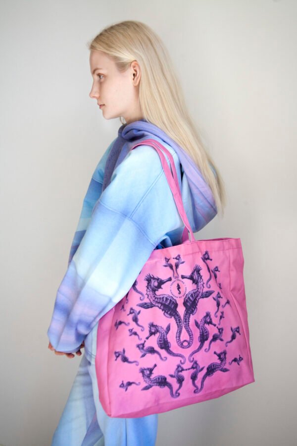 2. Woman wearing pink Mirage tote bag with seahorse design, dressed in blue and purple gradient outfit