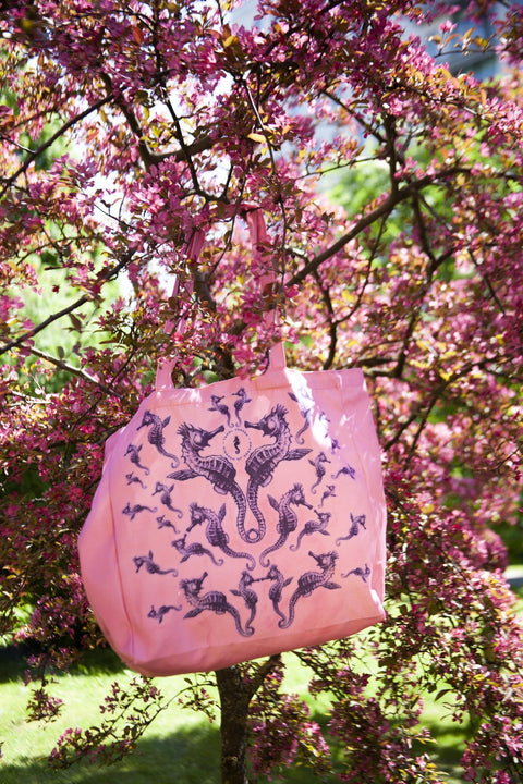 1. Pink Mirage tote bag with seahorse design hanging on a blooming tree branch