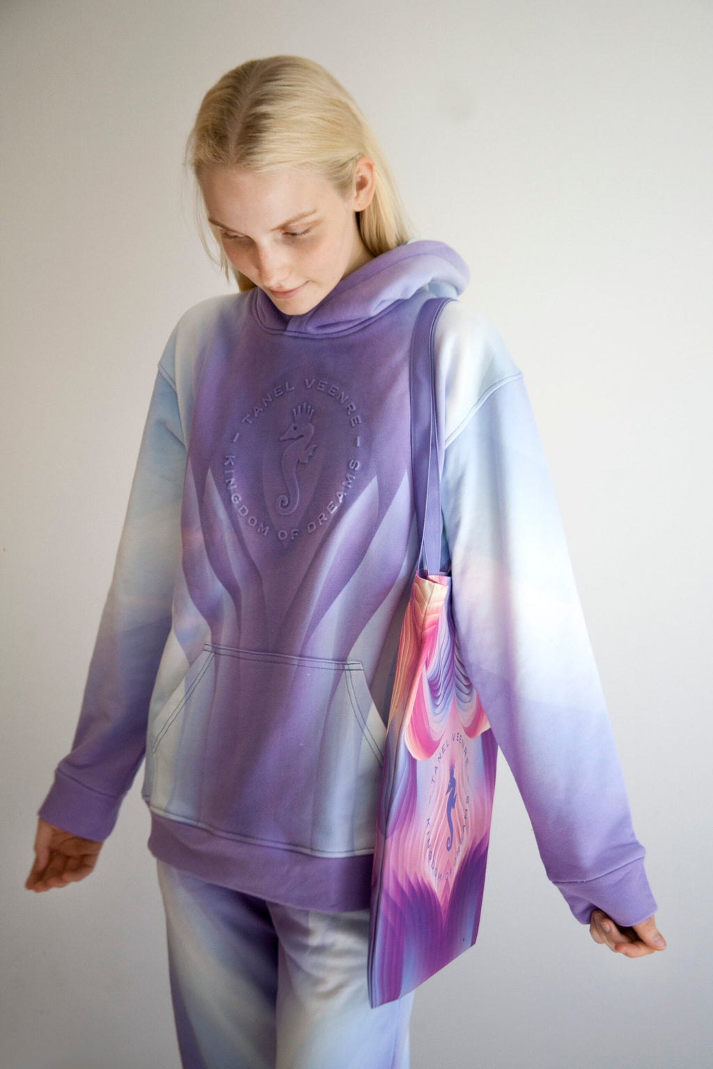 2. Woman in a gradient purple hoodie carrying a Tanel Veenre Mirage tote bag with a vibrant pink and purple pattern