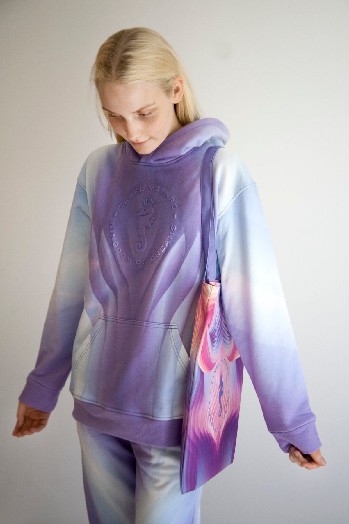 2. Woman in a gradient purple hoodie carrying a Tanel Veenre Mirage tote bag with a vibrant pink and purple pattern