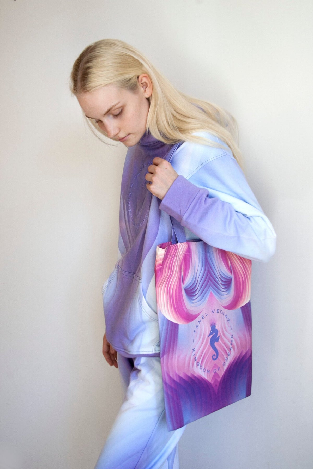 1. Woman wearing a pastel hoodie and pants holding a Tanel Veenre Mirage tote bag with a pink and purple seahorse design