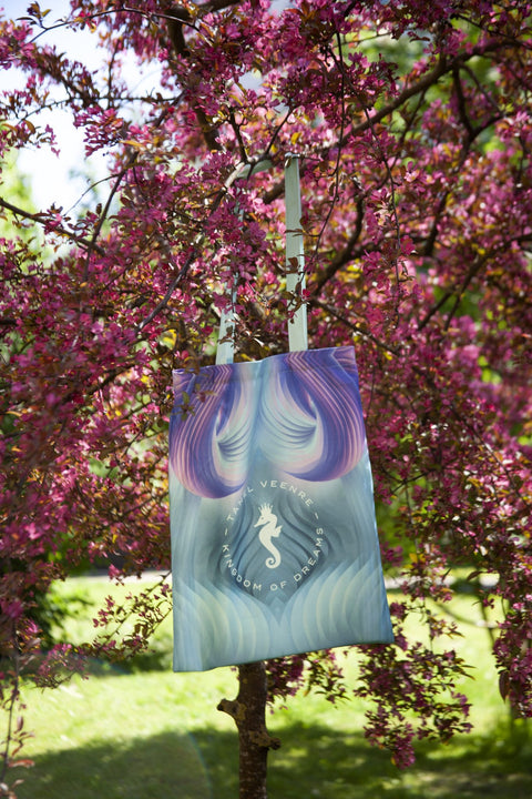 4. Tanel Veenre Mirage tote bag with a seahorse design hanging on a tree with pink blossoms in a garden setting