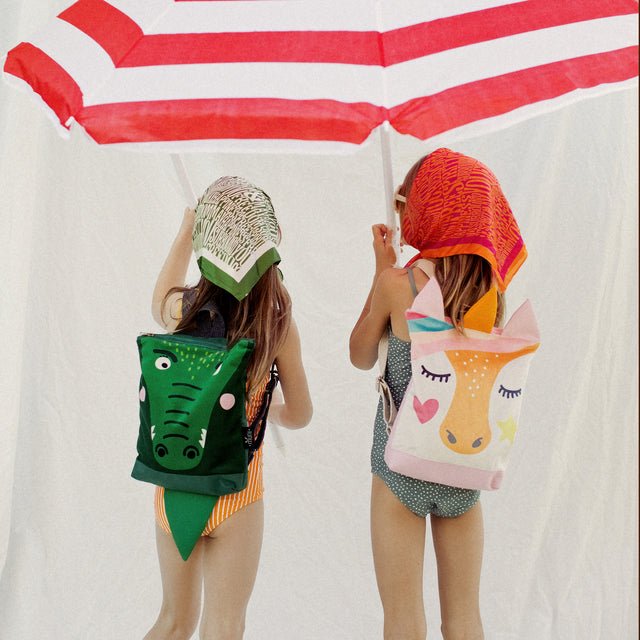 2. Two girls with Muni backpacks, crocodile and deer designs, under umbrella