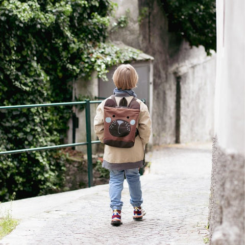 1. Child wearing Muni bear-shaped backpack on a cobblestone path, showcasing playful design