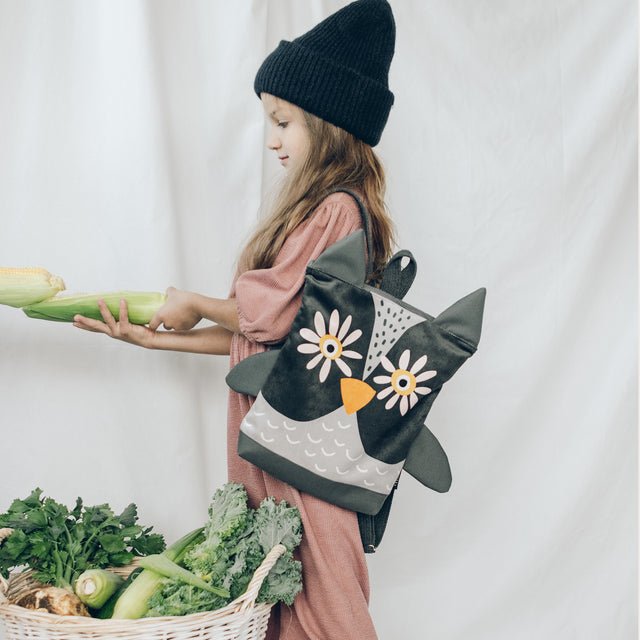 1. Girl wearing Muni kids owl backpack in lifestyle setting, holding vegetables