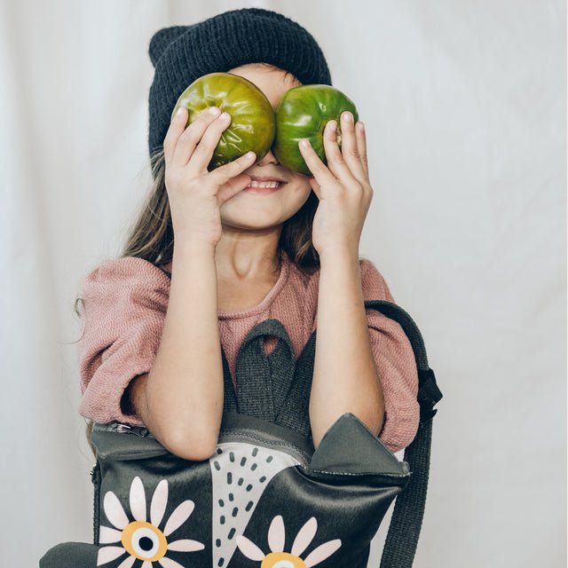 3. Girl playfully holding green tomatoes with Muni owl backpack in lifestyle setting