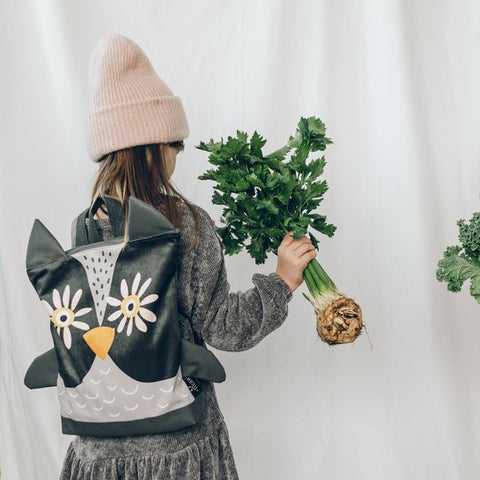 2. Girl with Muni owl backpack in lifestyle setting, holding celery