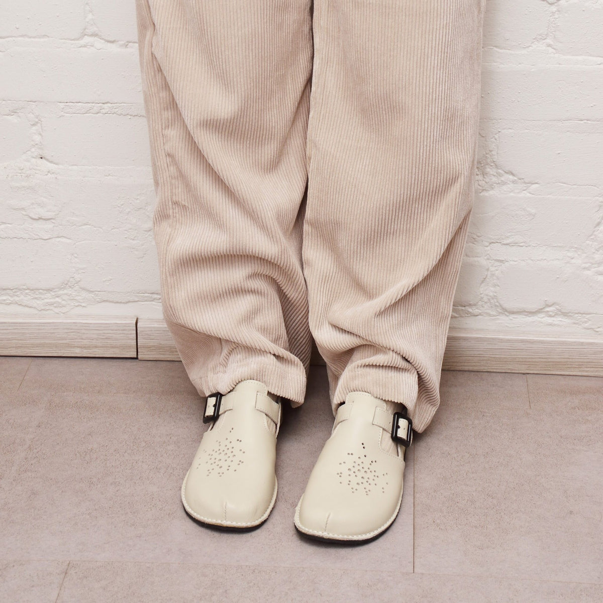 2. Close-up of Omaking Kuuda Shoes in white worn by a woman with beige corduroy pants, showing front view
