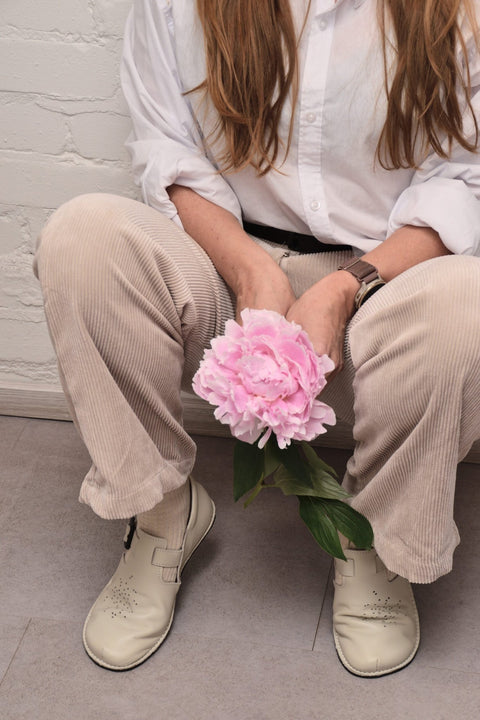 1. Woman wearing Omaking Kuuda Shoes in white, styled with beige corduroy pants, holding a pink flower