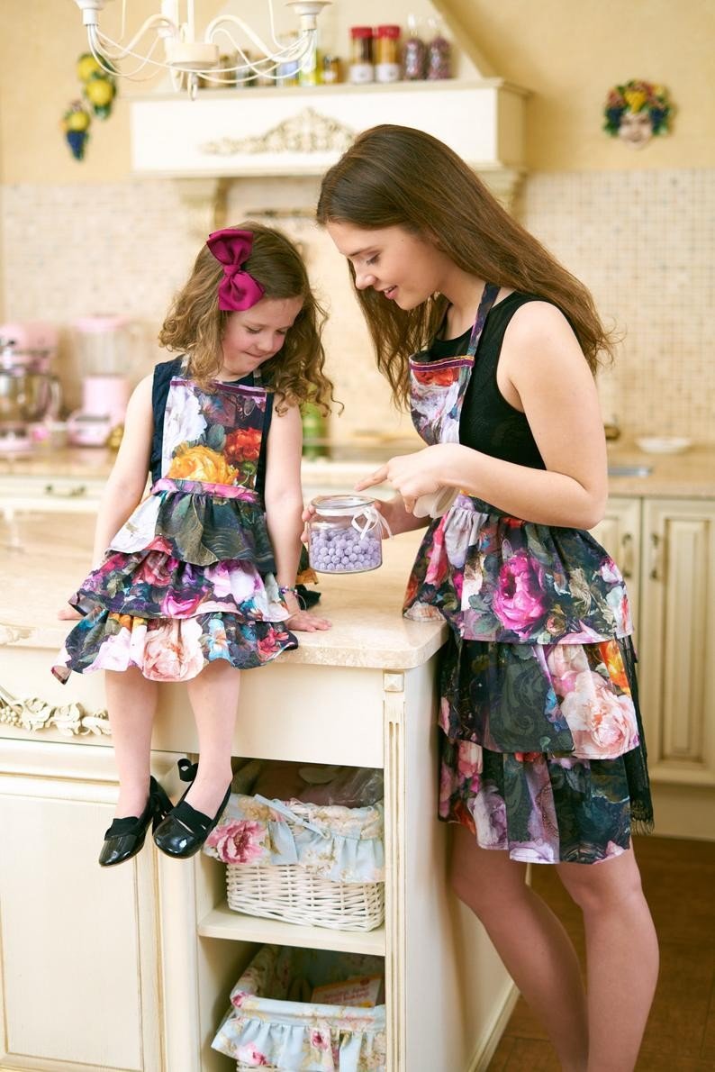 1. Woman and child in matching dark floral aprons with ruffles in a cozy kitchen setting