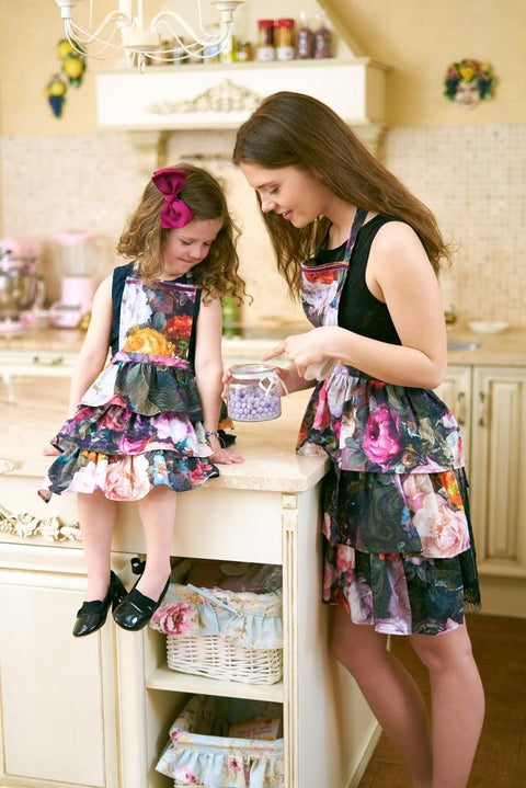 1. Woman and child in matching dark floral aprons with ruffles in a cozy kitchen setting