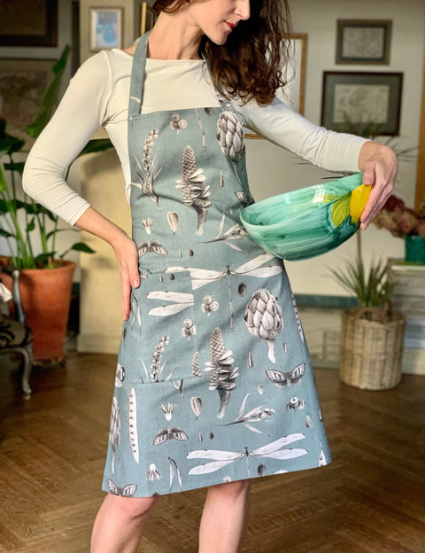 1. Woman modeling Hortensias Home Seeds Aqua apron with botanical design holding a decorative bowl indoors