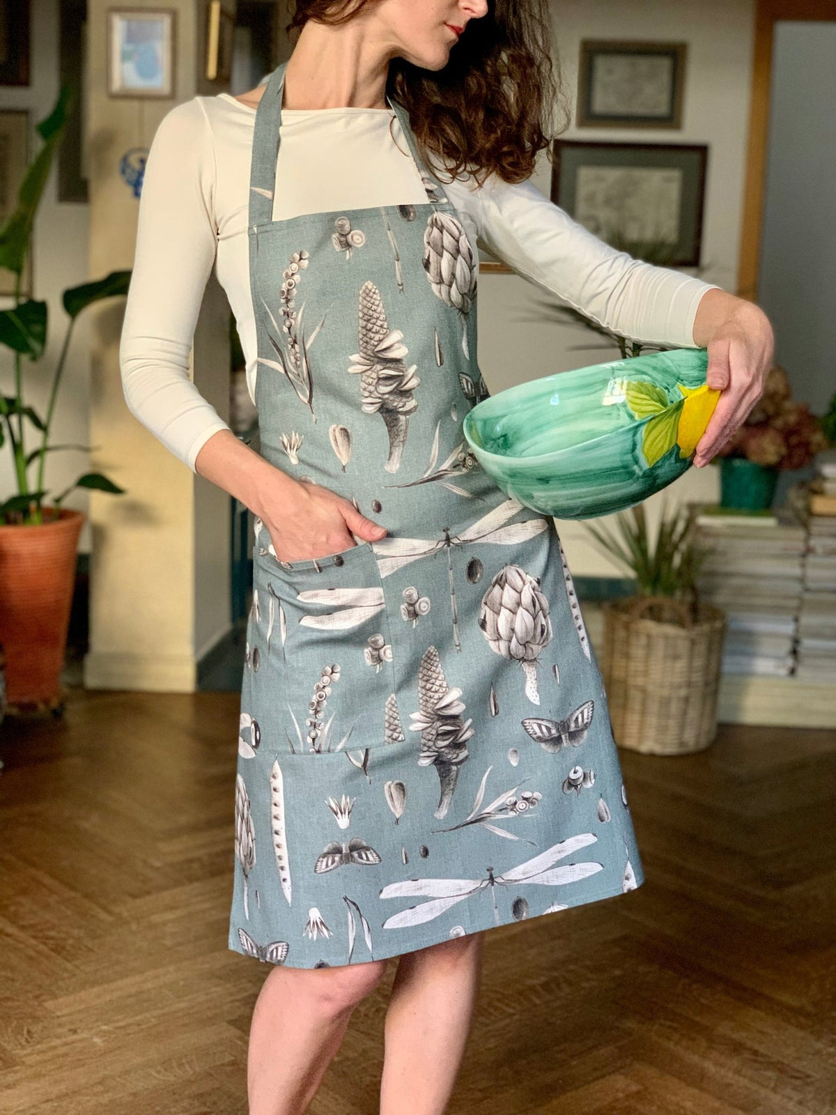 1. Woman wearing Hortensias Home Seeds Aqua apron holding a green bowl in a cozy kitchen setting