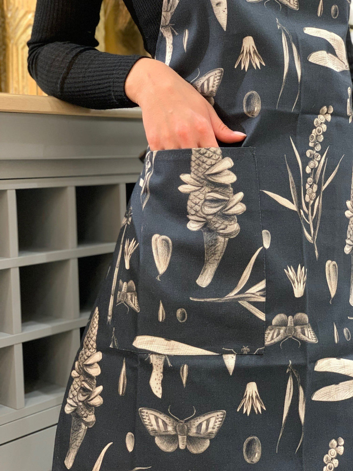 4. Partial view of Seeds Carbon apron pocket detail with botanical print, worn by a person in a black top