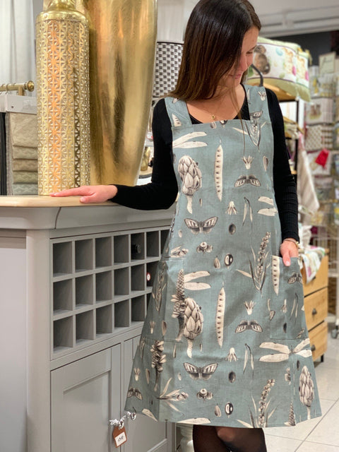 2. Woman wearing Seeds Aqua print apron with crossed straps, standing in a home interior