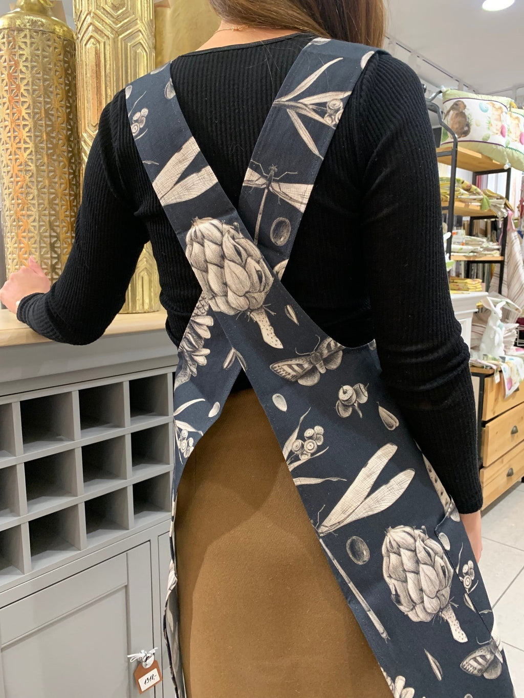 1. Woman wearing Hortensias Home Seeds Carbon apron with crossed straps in a store setting