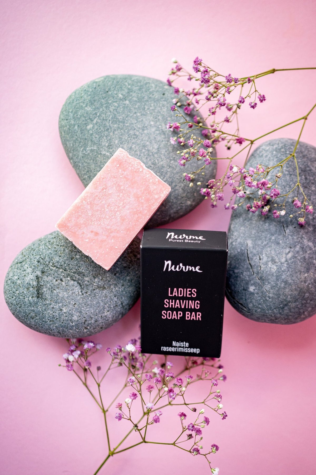4. Flat lay of Nurme Ladies Shaving Soap Bar with pink soap and black packaging on pink background with stones and flowers