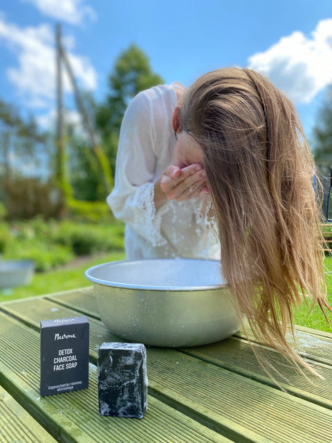 1. Woman washing face outdoors with Nurme Detox Charcoal Face Soap beside metal bowl