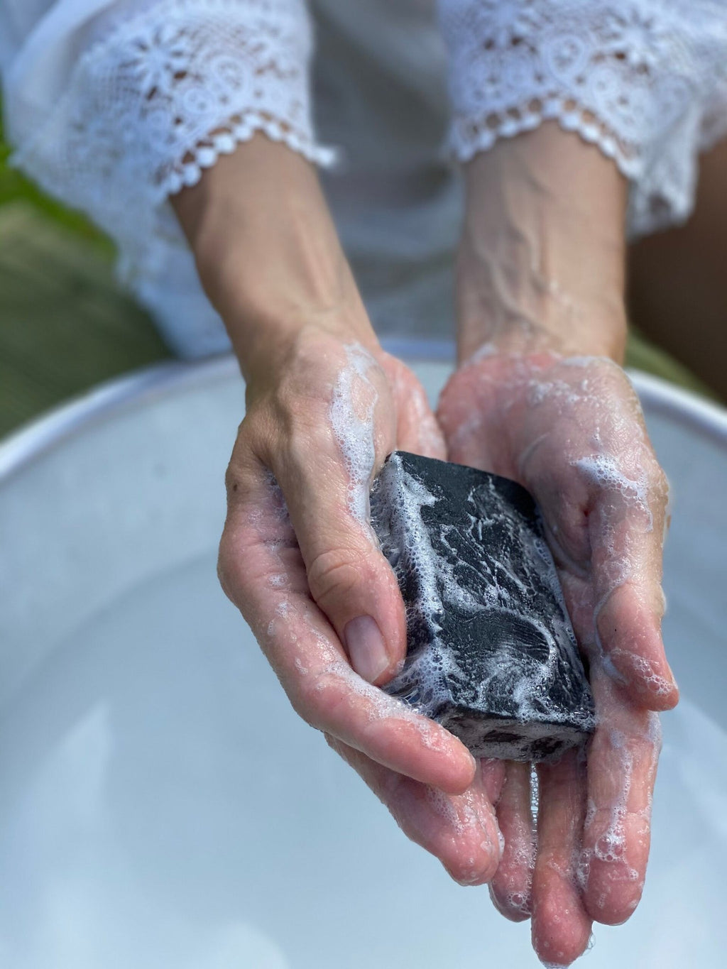 3. Close-up of hands holding lathered Nurme Detox Charcoal Face Soap over water