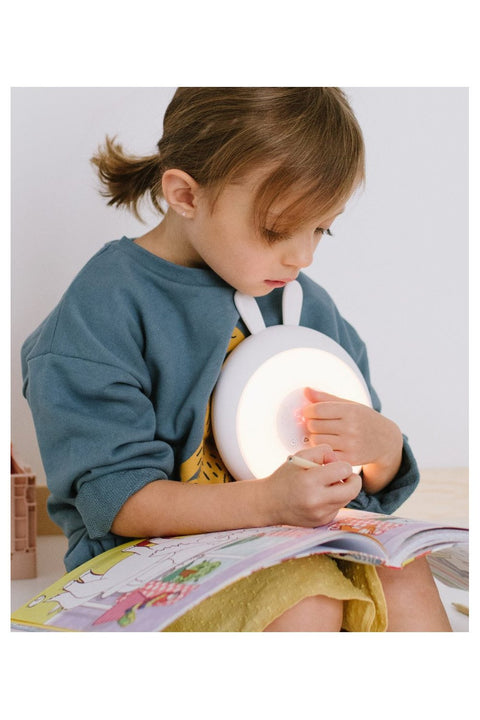 1. Young girl holding white Rabbit & Friends alarm clock lamp with rabbit ears while reading a book
