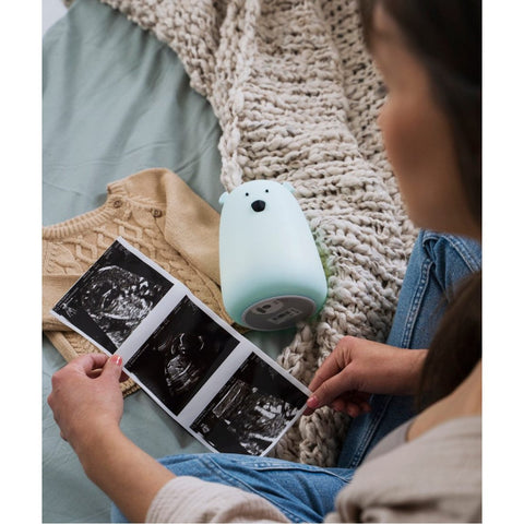 1. Woman looking at ultrasound images with blue teddy bear lamp on bed