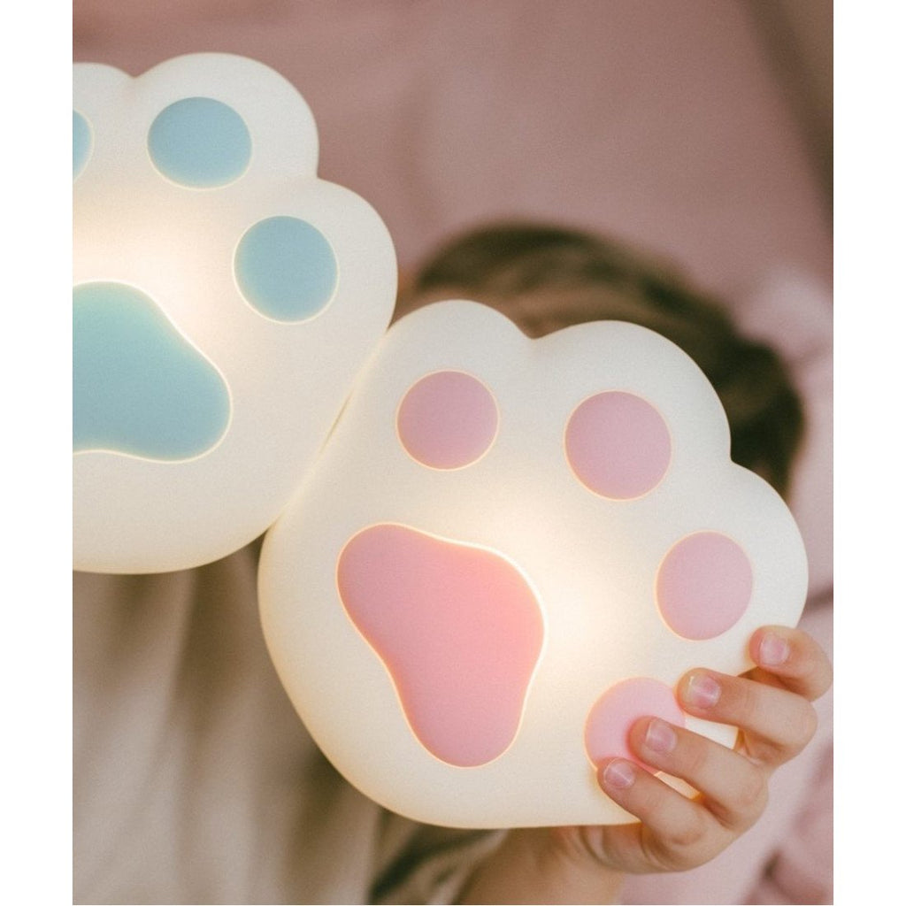 2. Child holding two paw-shaped silicone lamps, one pink and one blue, in a playful setting