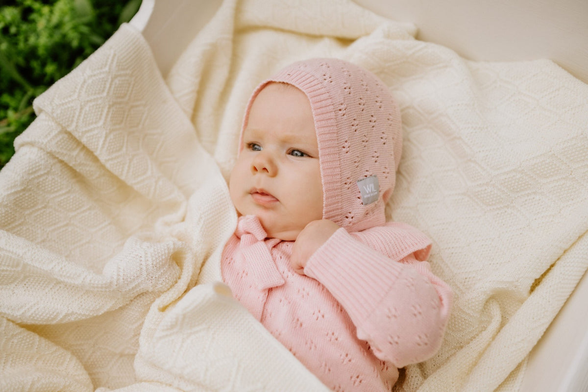 3. Baby lying on cream merino wool blanket wearing pink romper and bonnet