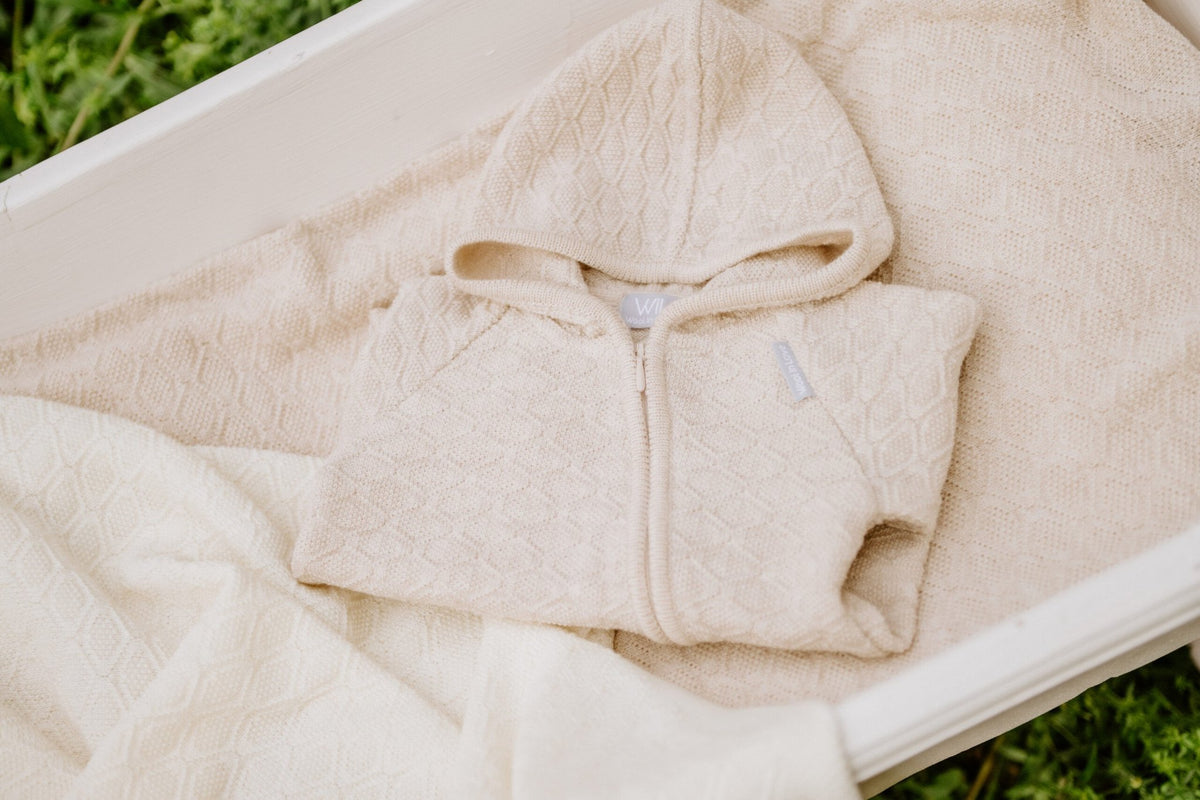 8. Beige merino wool romper folded on matching blanket in white bassinet