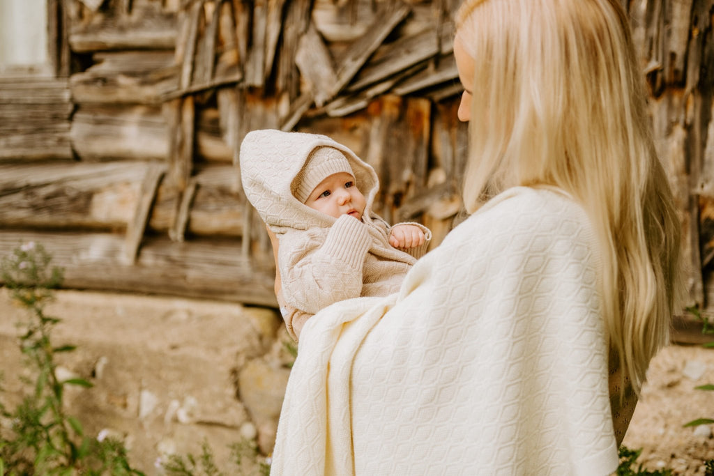 6. Woman holding baby in beige merino wool romper and bonnet with matching blanket outdoors