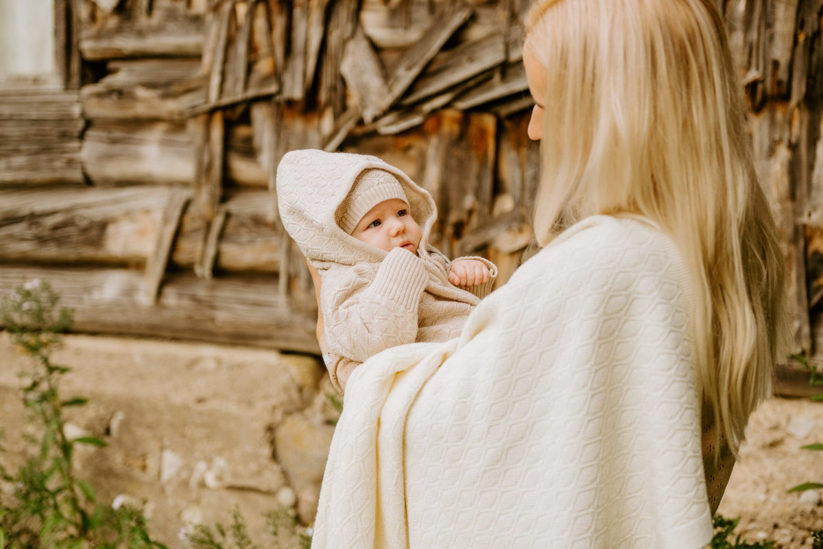 6. Woman holding baby in beige merino wool romper and bonnet with matching blanket outdoors