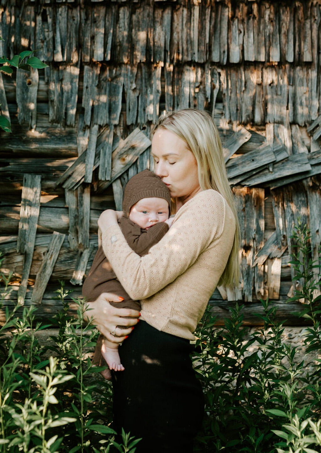5. Woman holding baby in brown merino wool romper and bonnet against rustic wooden background