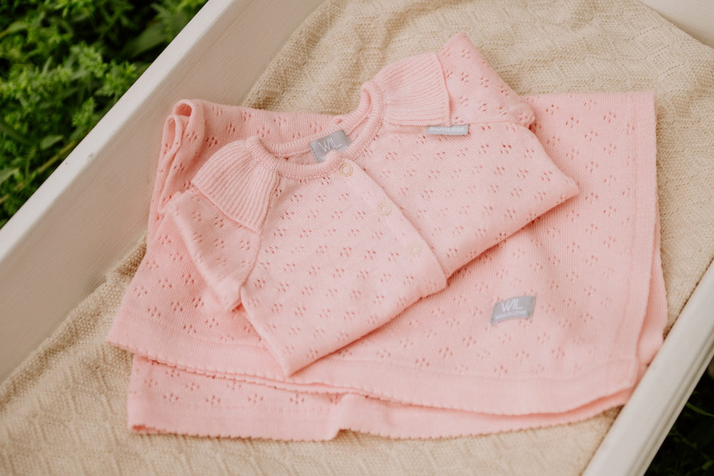 9. Pink merino wool romper and blanket set displayed in a cradle