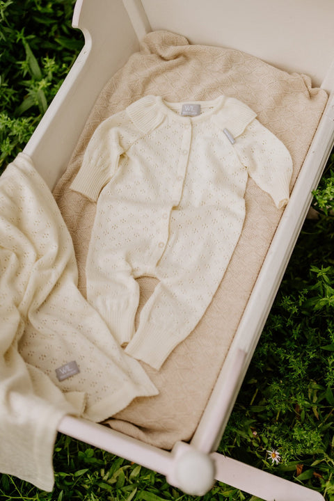 2. Cream merino wool romper and blanket set displayed in a white cradle