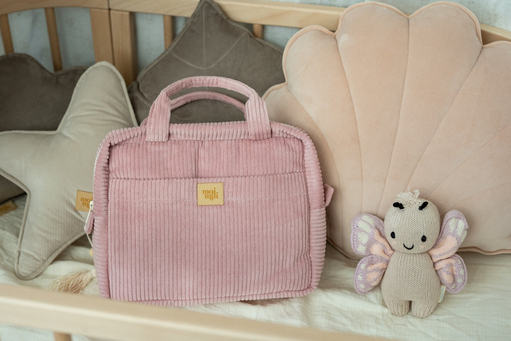 1. Baby pink makeup bag by Moi Mili on a crib with plush toys and pillows