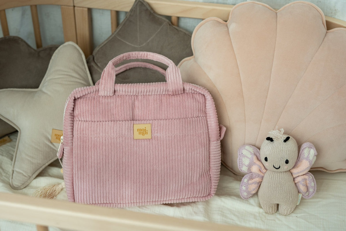 1. Baby pink makeup bag by Moi Mili on a crib with plush toys and pillows