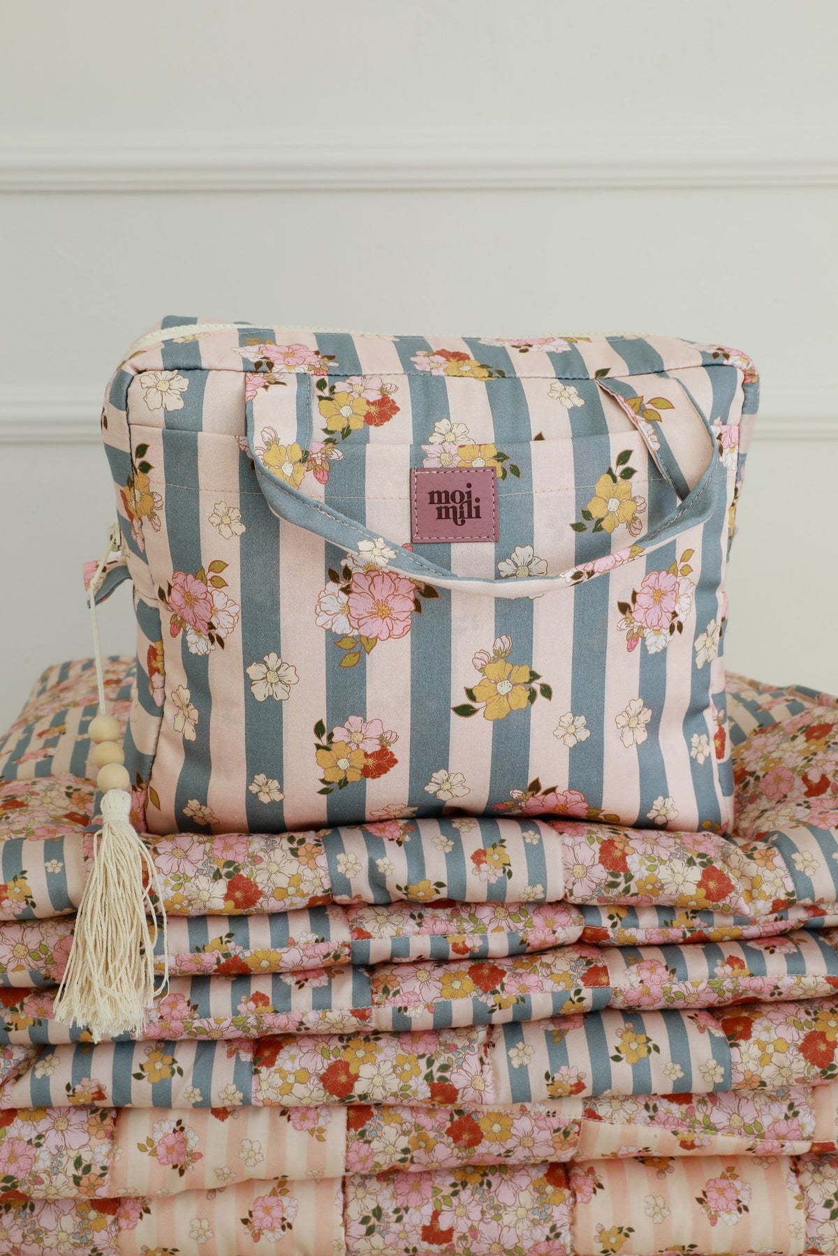 4. Blue striped makeup bag with floral print and Moi Mili logo, placed on matching floral fabric stack