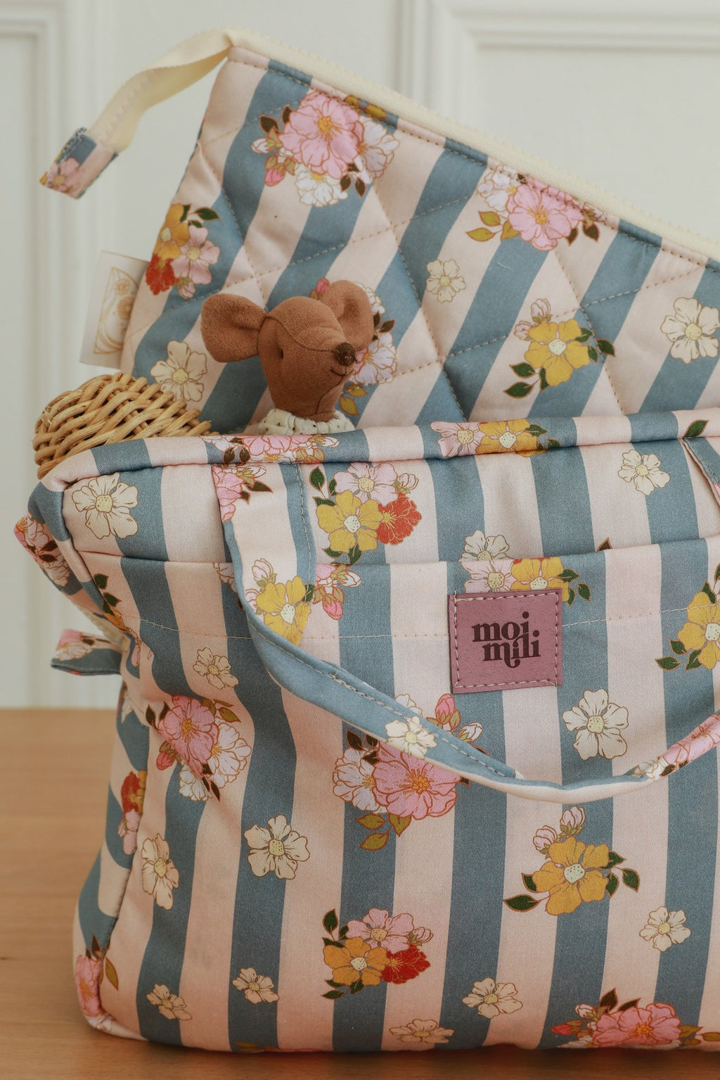 2. Close-up of blue striped makeup bags with floral print, featuring a small toy peeking out and moi mili logo visible