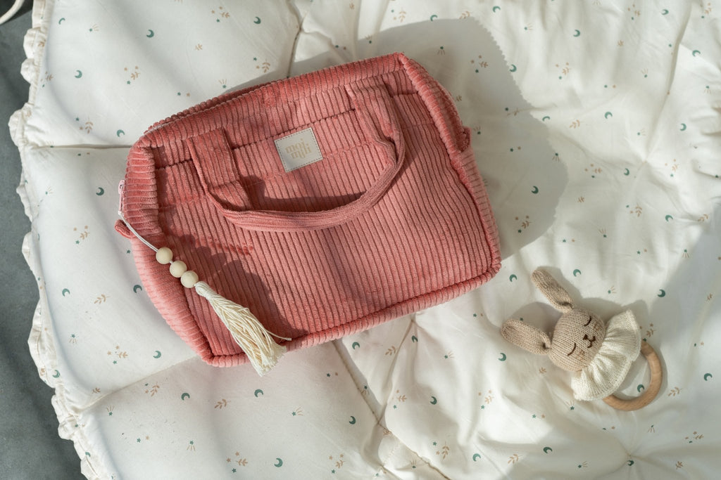 6. Large coral makeup bag with tassel detail on a quilted blanket next to a toy rabbit