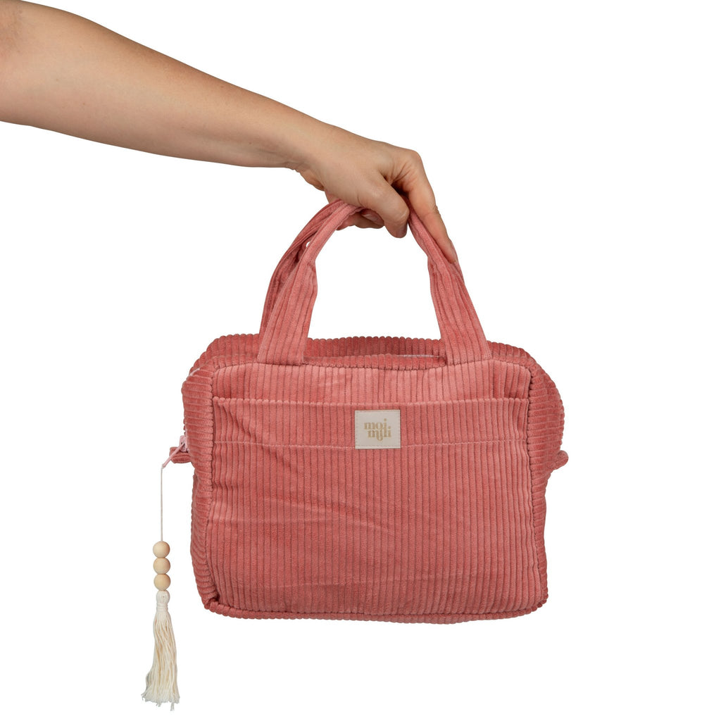2. Hand holding large coral makeup bag with handles and tassel detail, showcasing size and design