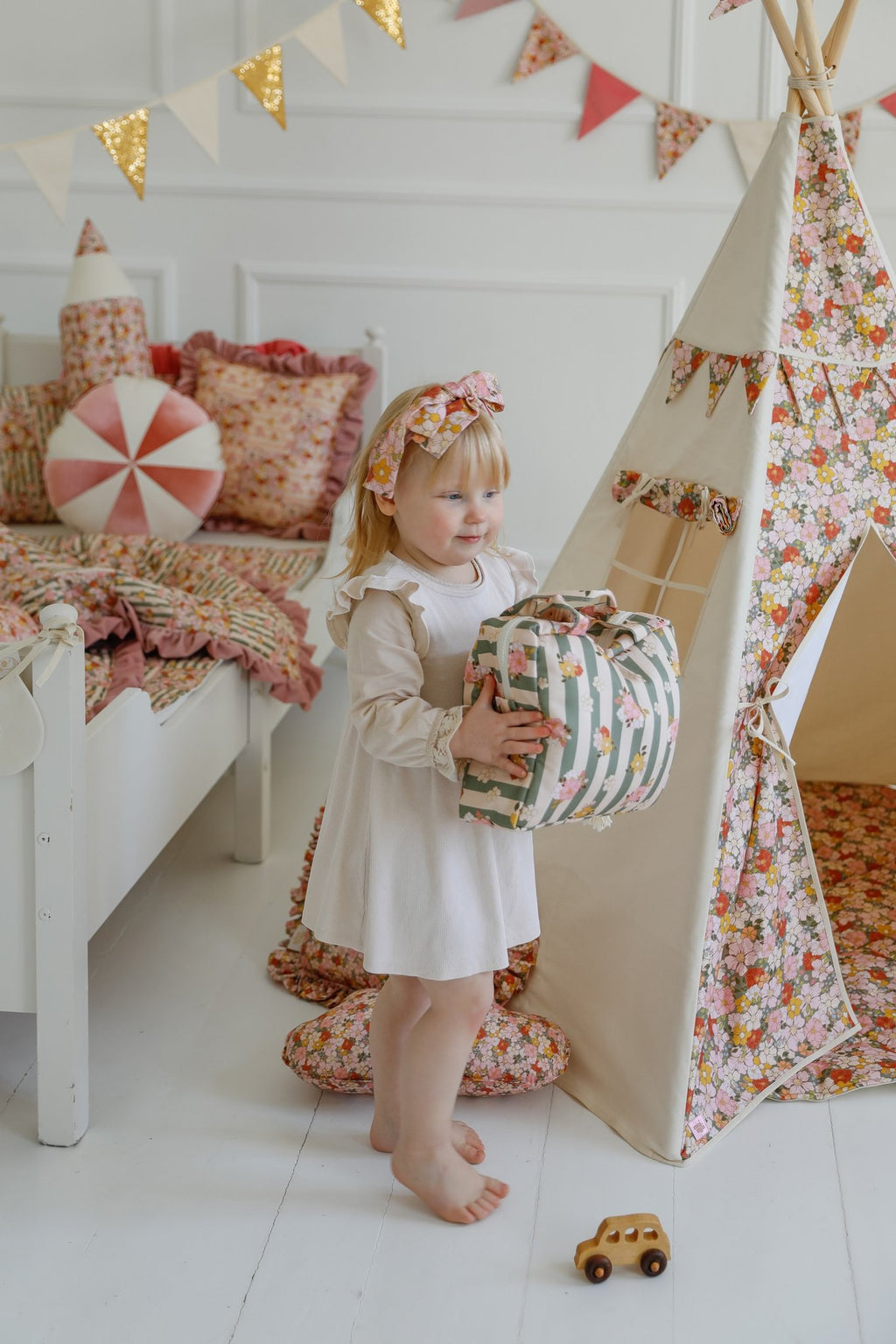 2. Young girl holding green striped large make-up bag with floral design in a playroom with a floral teepee