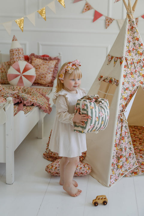 2. Young girl holding green striped large make-up bag with floral design in a playroom with a floral teepee