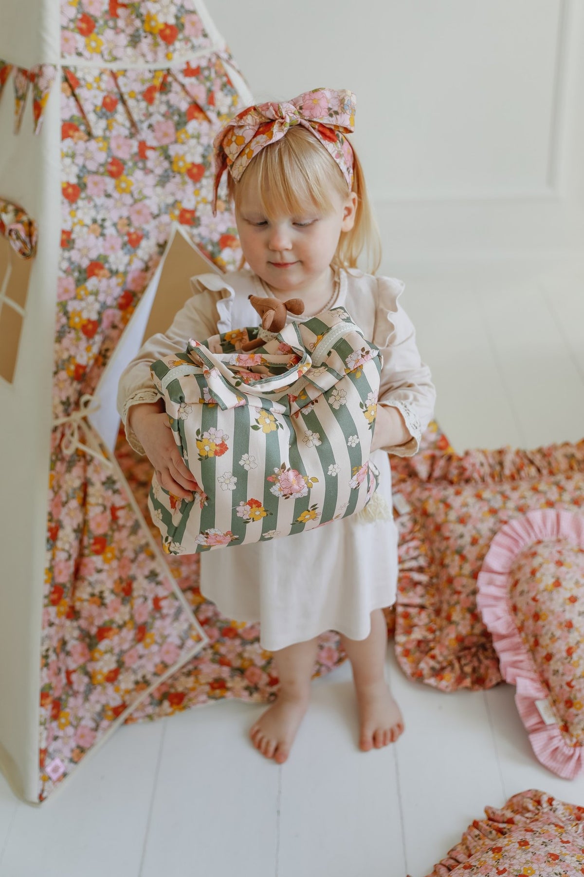 4. Young girl holding green striped large make-up bag with floral design in a playroom with floral decor
