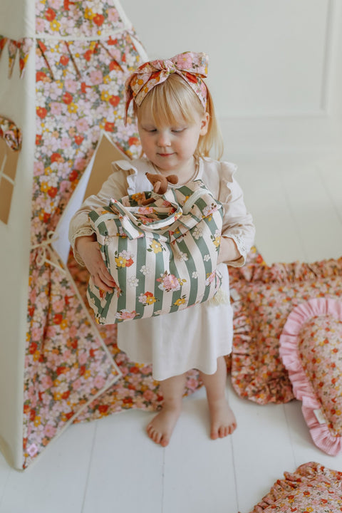 4. Young girl holding green striped large make-up bag with floral design in a playroom with floral decor