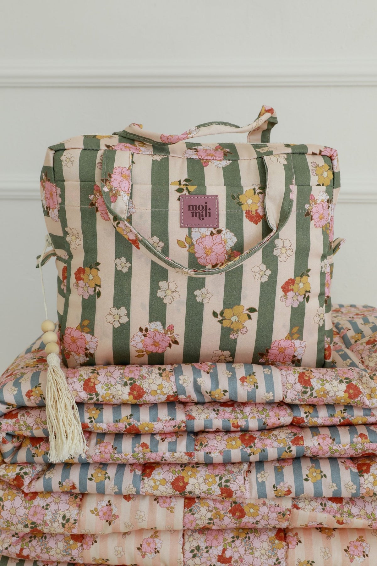 1. Green striped large make-up bag with floral pattern and tassel detail on a stack of matching quilts in a cozy room
