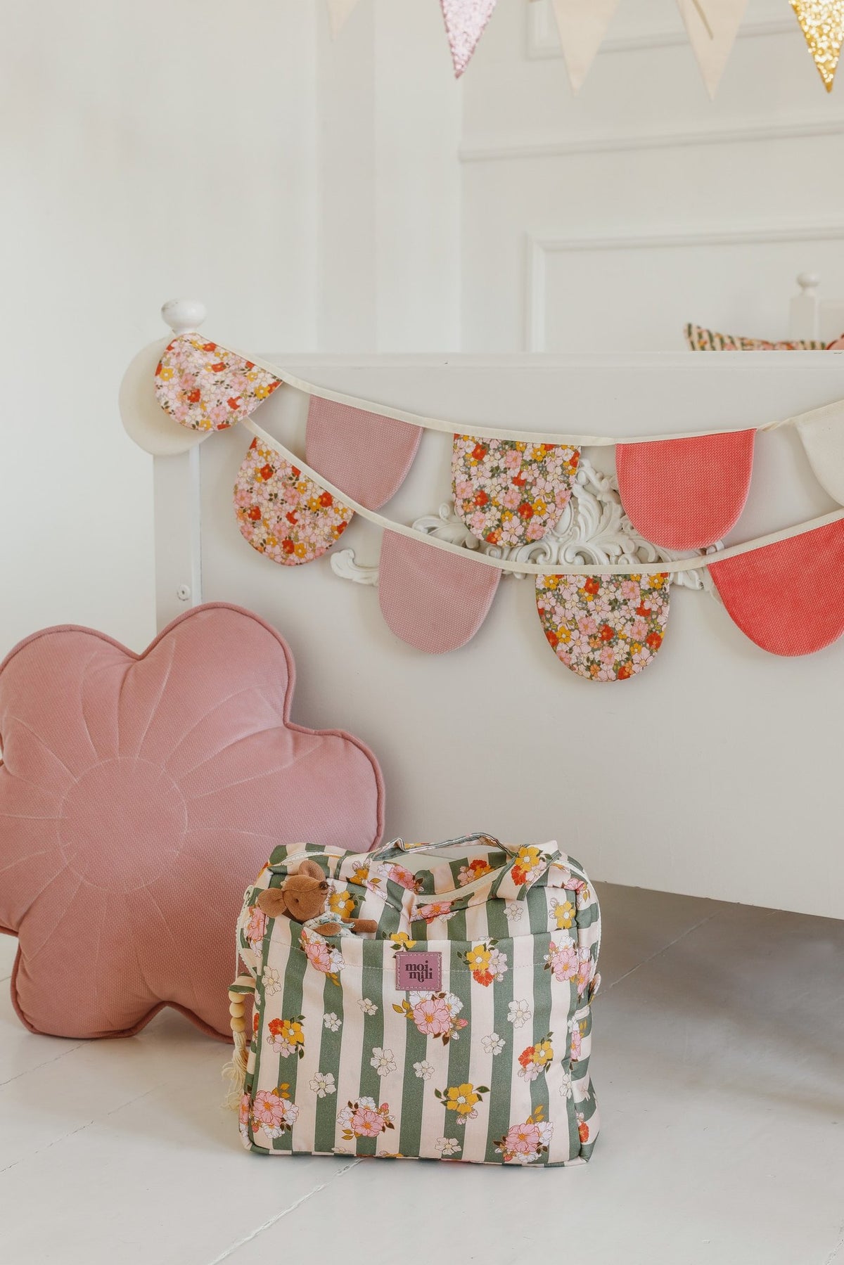 5. Green striped large make-up bag with floral pattern next to a pink flower-shaped cushion under a decorated bed