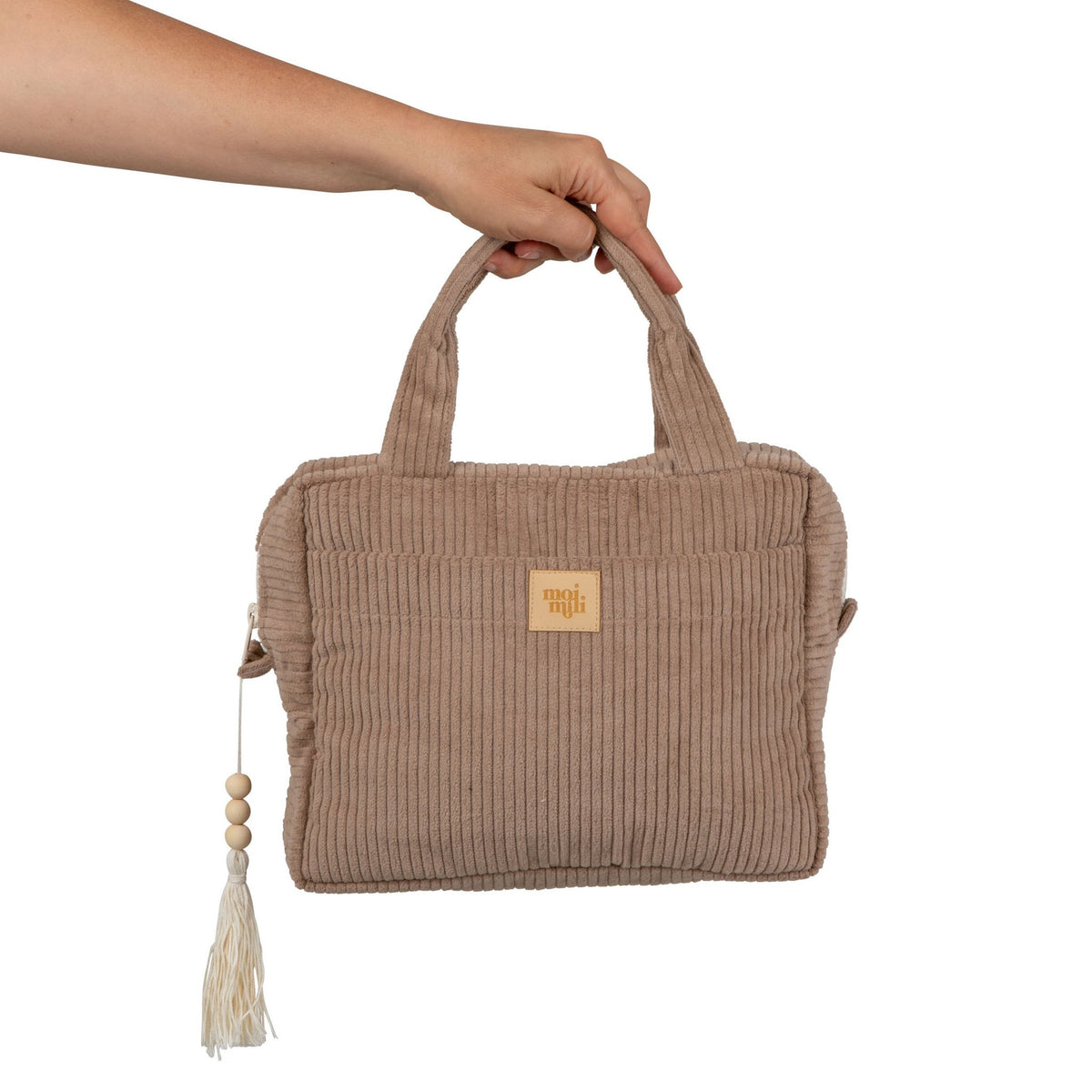 3. Hand holding latte-colored large makeup bag with Moi Mili logo and tassel detail, showcasing size and portability.